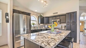 A modern kitchen with dark cabinets, stainless steel appliances, and a marble island with stools. - Close to Spring Training! Serene Retreat in Gibert (Gilbert)