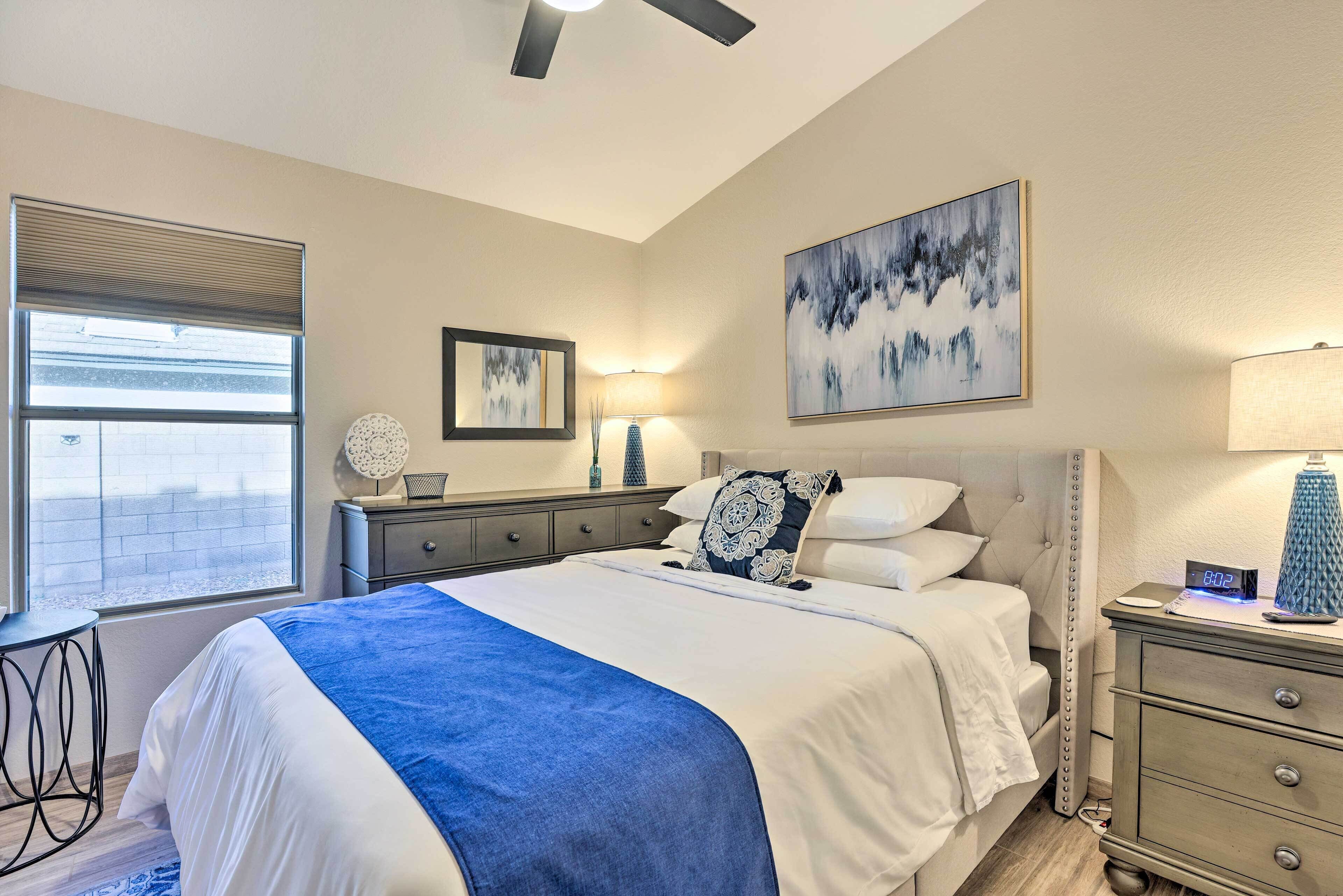 A bedroom with a bed, bedside tables, a ceiling fan, a window, and artwork on the walls.