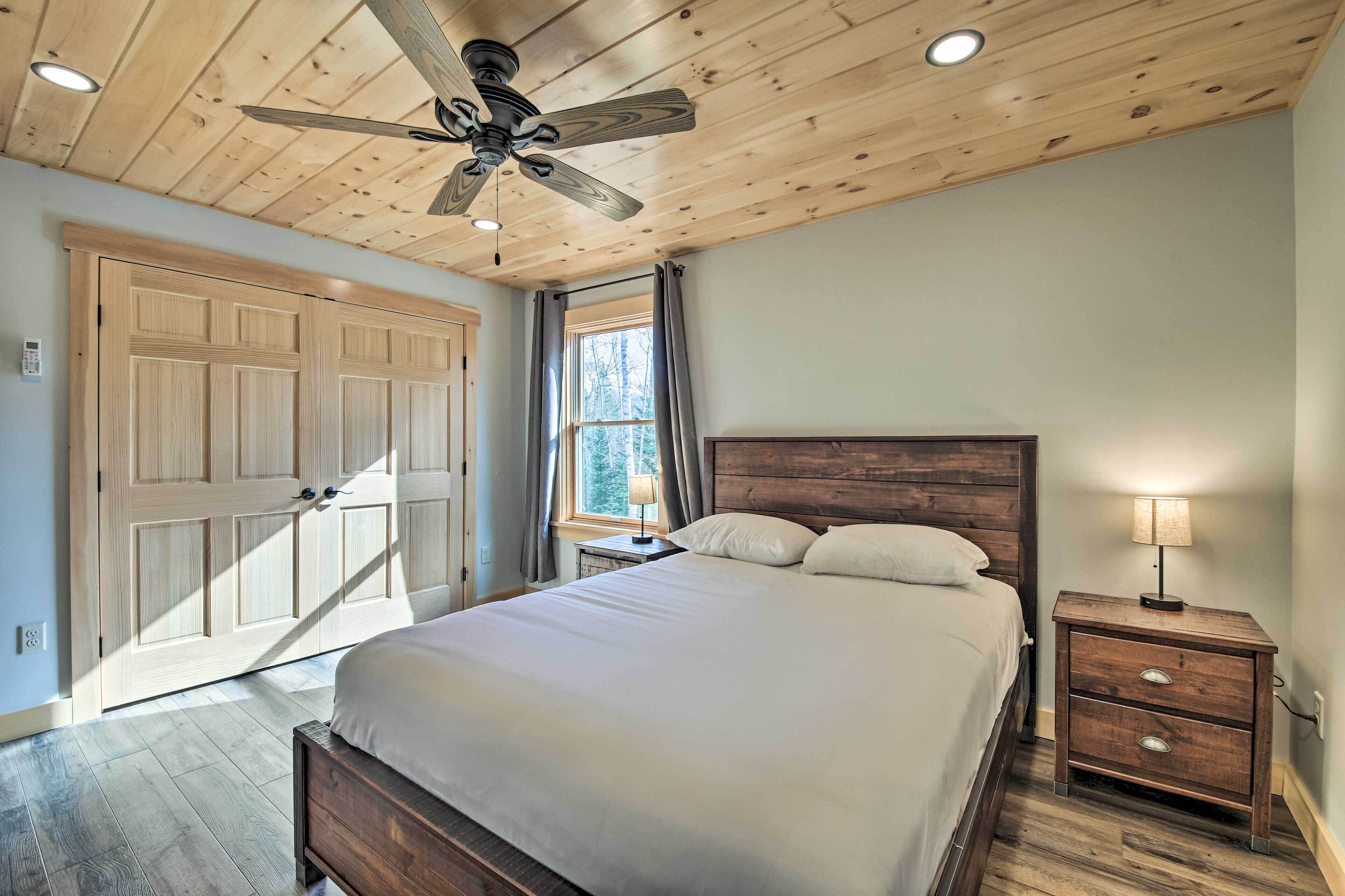 A bedroom with a wooden ceiling, a bed, a nightstand with a lamp, and a window with curtains.