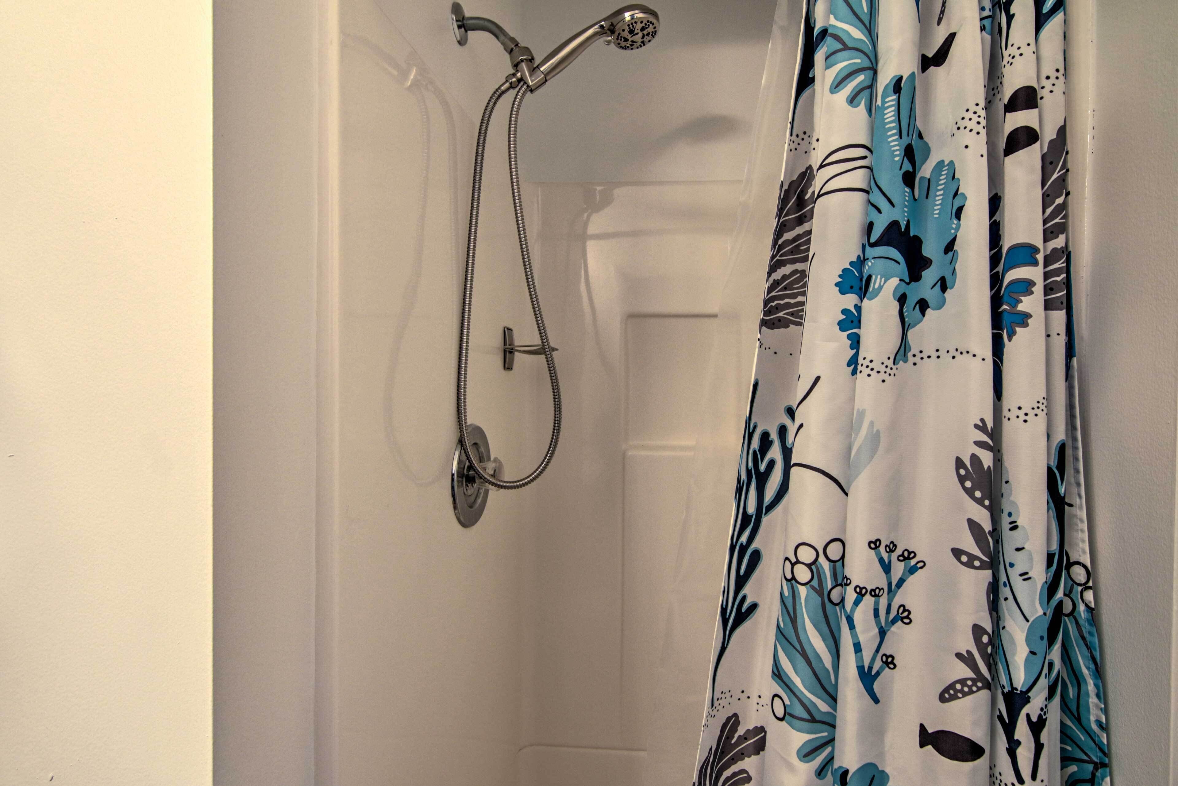 Une salle de bain avec une douche, une porte blanche et un rideau orné d’un motif floral bleu et noir.