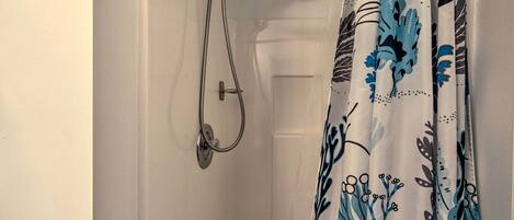 Une salle de bain avec une douche, une porte blanche et un rideau orné d’un motif floral bleu et noir.