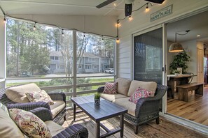 A covered porch with wicker furniture, a table, and a view of houses through large windows. - Cozy Family Townhome: 1 Mi to Bethanys Boardwalk (Bethany Beach)