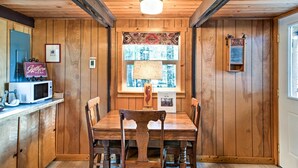 A wooden-paneled room with a dining table and chairs, a microwave, a sign reading "Caterpillar Here," and a window with patterned curtains. - Serene Washington Escape w/ Deck & Mountain Views! (Packwood)