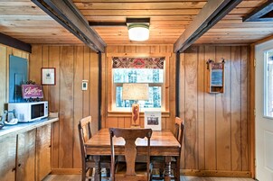 Una habitación con paneles de madera, una mesa de comedor y sillas, un microondas, un letrero que dice 'Caterpillar Here' y una ventana con cortinas estampadas.