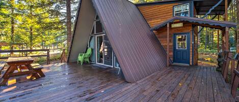 A wooden cabin with a slanted roof, a picnic table, and a door with a sign.