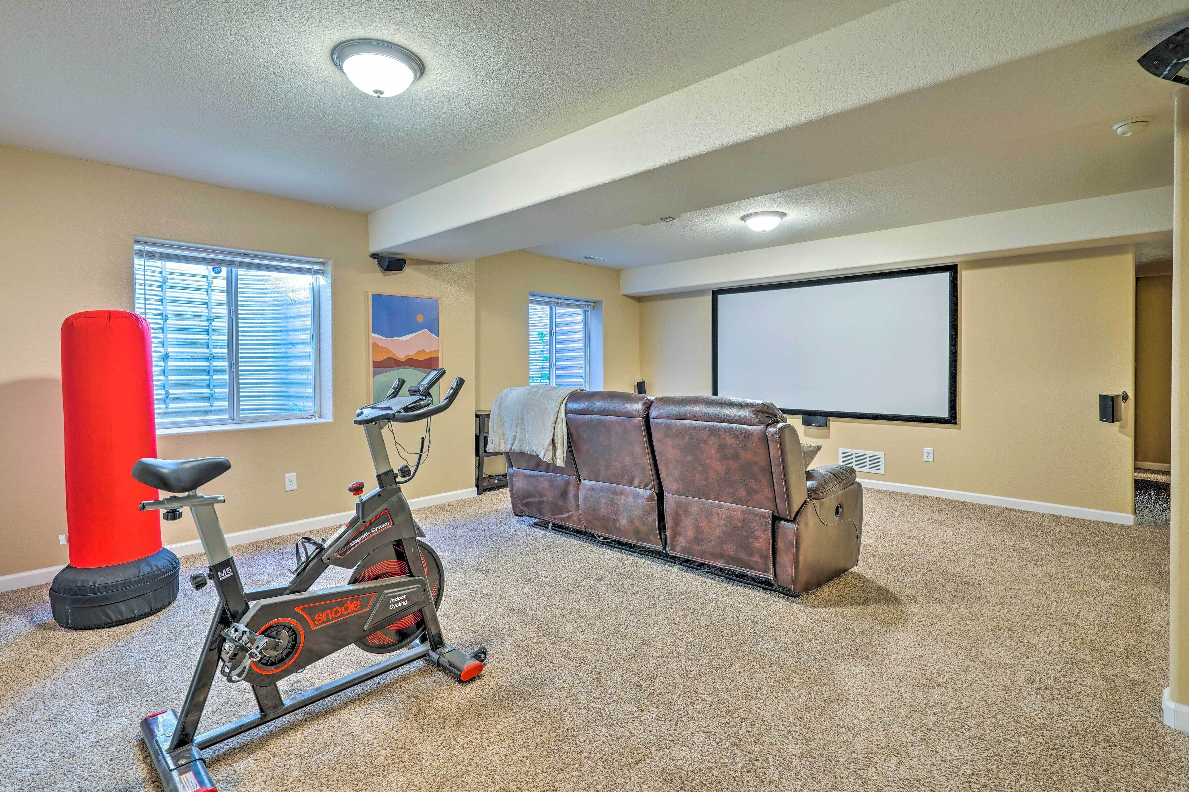 A home entertainment room with a large screen, a leather couch, and an exercise bike.
