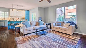 A spacious living room with a large window, a ceiling fan, and a kitchen area with blue cabinets. - Spacious Springs Home + Patio ~ 10 Mi to Dtwn (Colorado Springs)