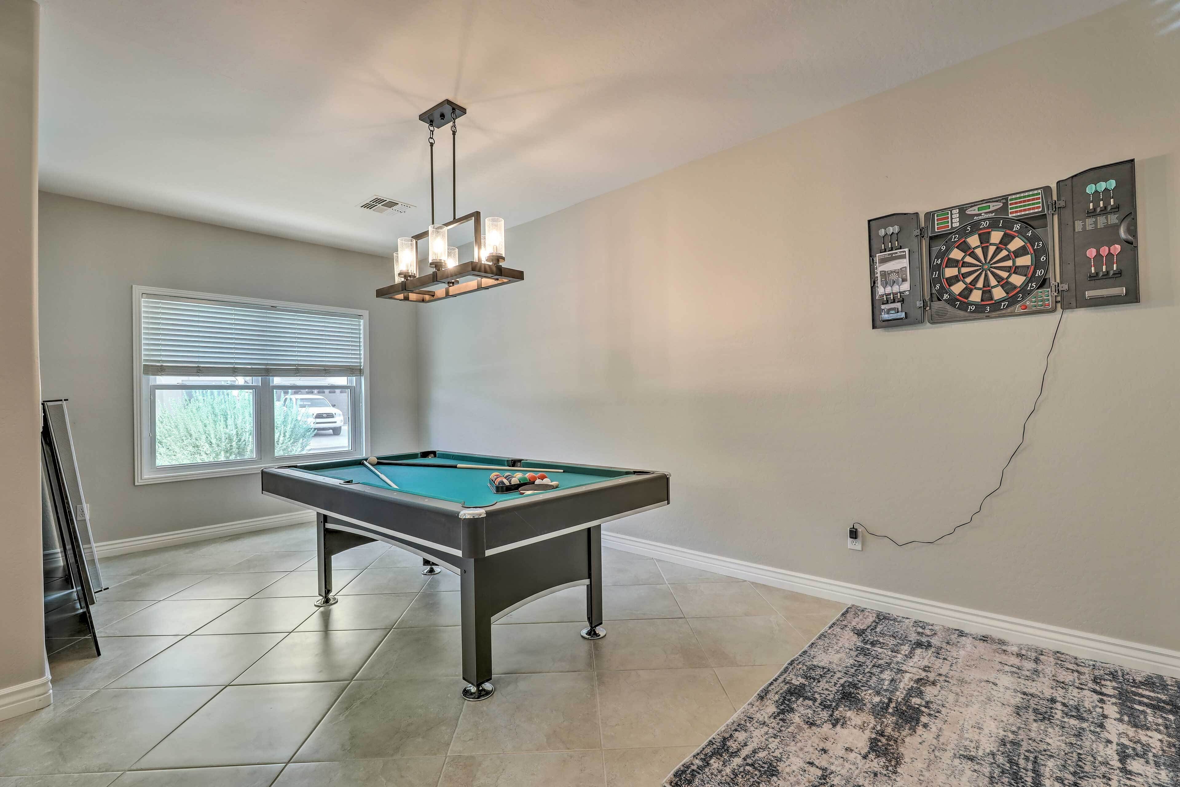Une table de billard dans une pièce où se trouvent un jeu de fléchettes et un lustre.