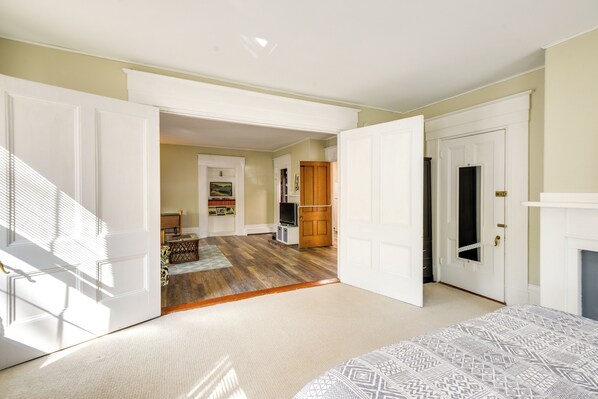 A spacious room with a large bed, a wooden floor, and a view of a dining area through an open door. - Kennebunk Apartment w/ Local Beach Access! (Kennebunk)