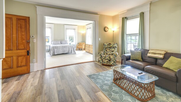 A spacious living room with a wooden floor, a glass coffee table, a brown leather sofa, and a patterned armchair. - Kennebunk Apartment w/ Local Beach Access! (Kennebunk)
