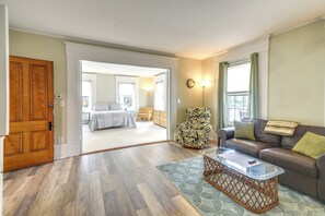 A spacious living room with a wooden floor, a glass coffee table, a brown leather sofa, and a patterned armchair. - Kennebunk Apartment w/ Local Beach Access! (Kennebunk)