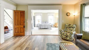A spacious living room with hardwood flooring, a large armchair, a sofa, and a view into the bedroom through an open door. - Kennebunk Apartment w/ Local Beach Access! (Kennebunk)