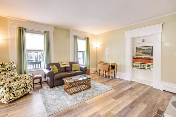 A living room with a brown sofa, patterned armchair, and a coffee table. - Kennebunk Apartment w/ Local Beach Access! (Kennebunk)