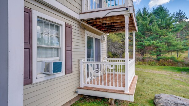 Uma casa com varanda coberta, janela com aparelho de ar condicionado e vista para uma área arborizada.