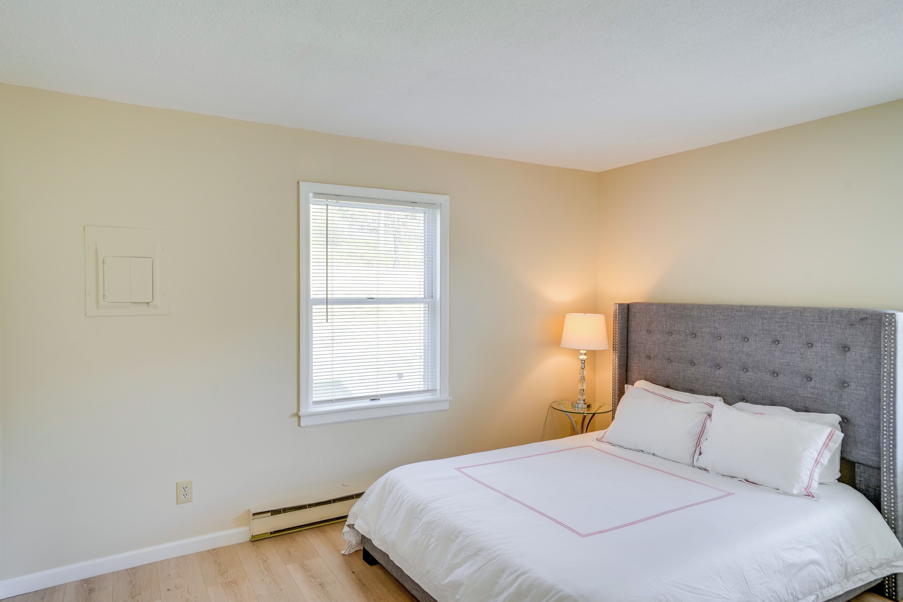 A bedroom with a bed, a nightstand, a lamp, and a window with blinds.