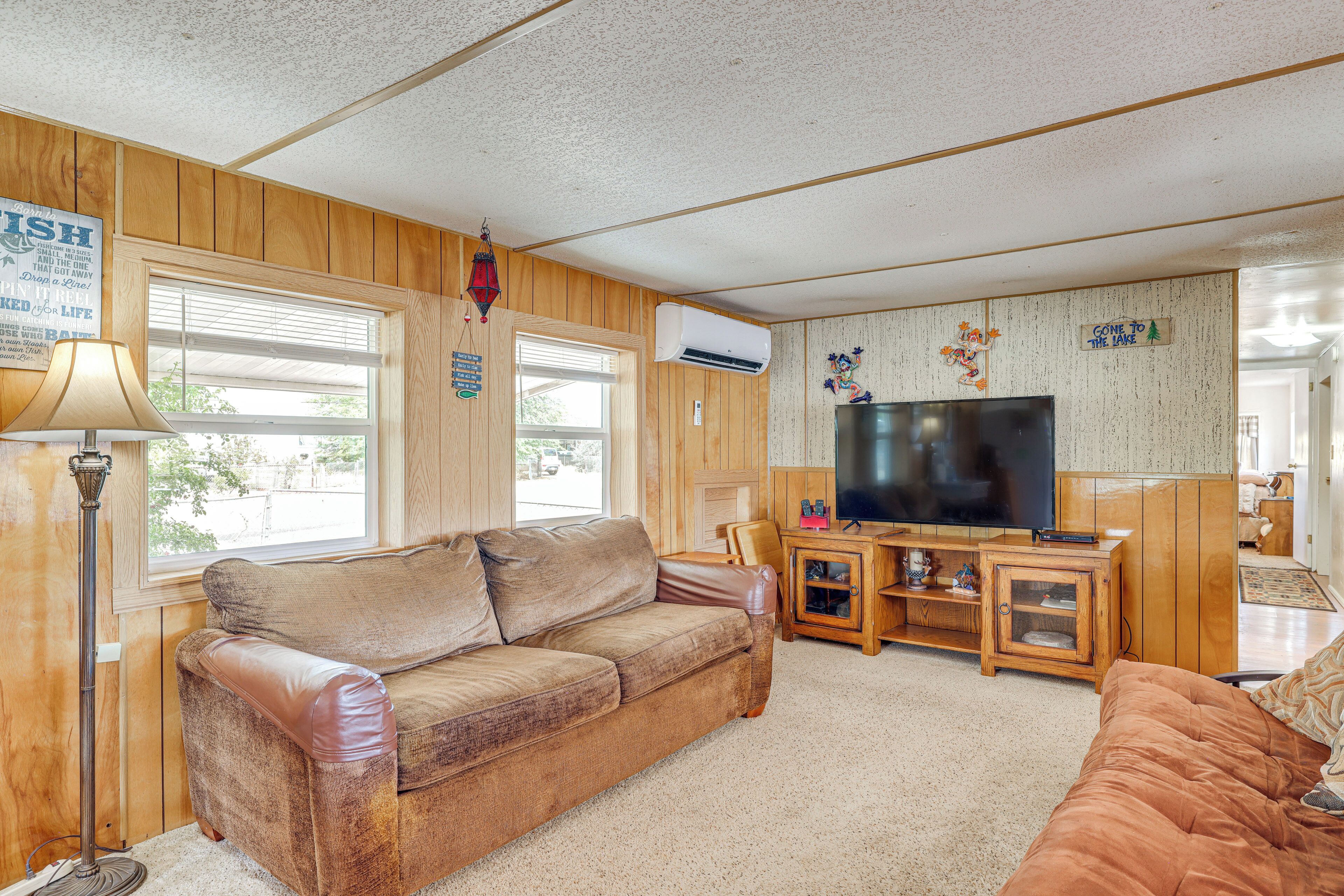 A cozy living room with a wooden floor, a brown leather sofa, a television, and a wall-mounted air conditioner.
