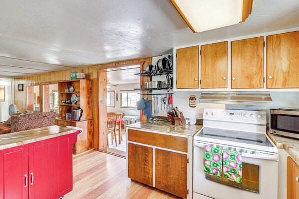 Cocina compacta con armarios de madera, encimera roja y estufa de estilo antiguo.