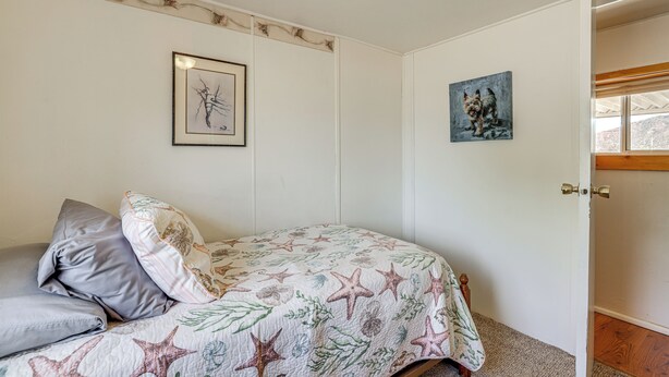 Een slaapkamer met een bed, een kussen, een ingelijst schilderij en een deur.