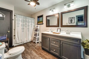 Un bagno con il water, un mobile lavabo con specchio, una tenda da doccia e una ventola a soffitto.