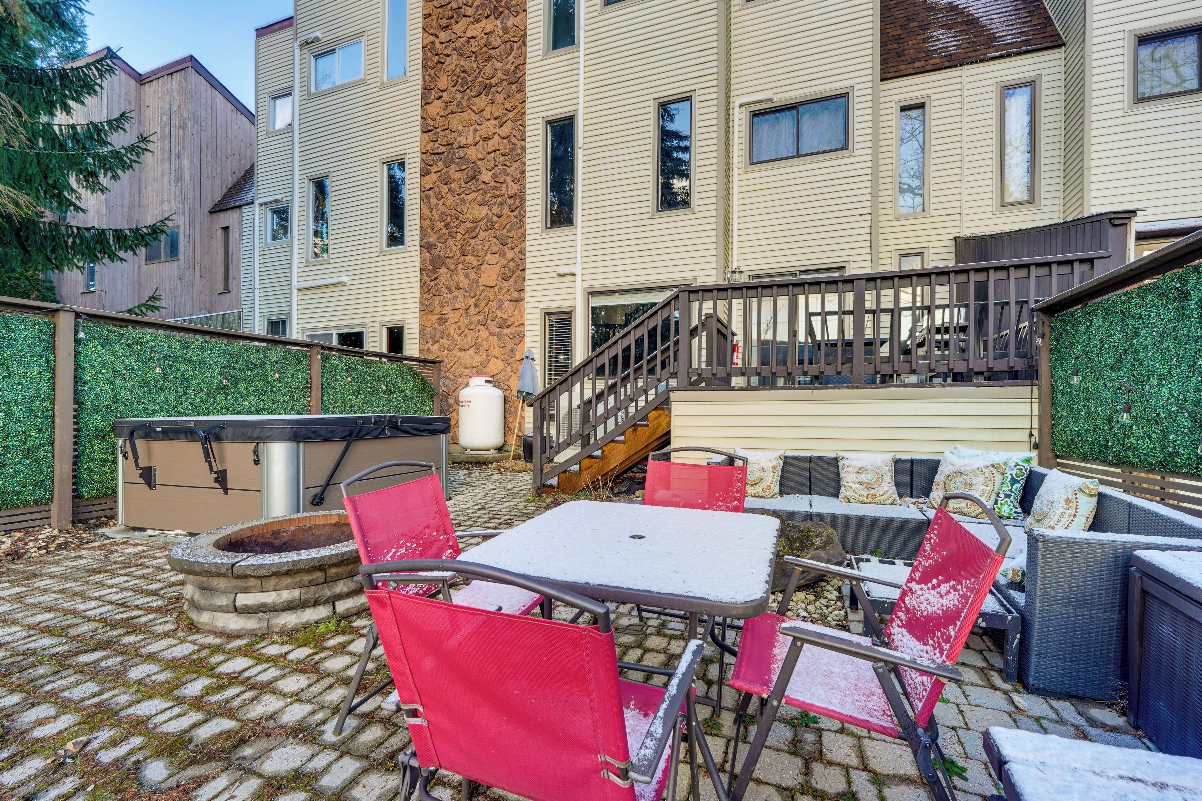 An outdoor patio area with a stone fire pit, red chairs, and a table.