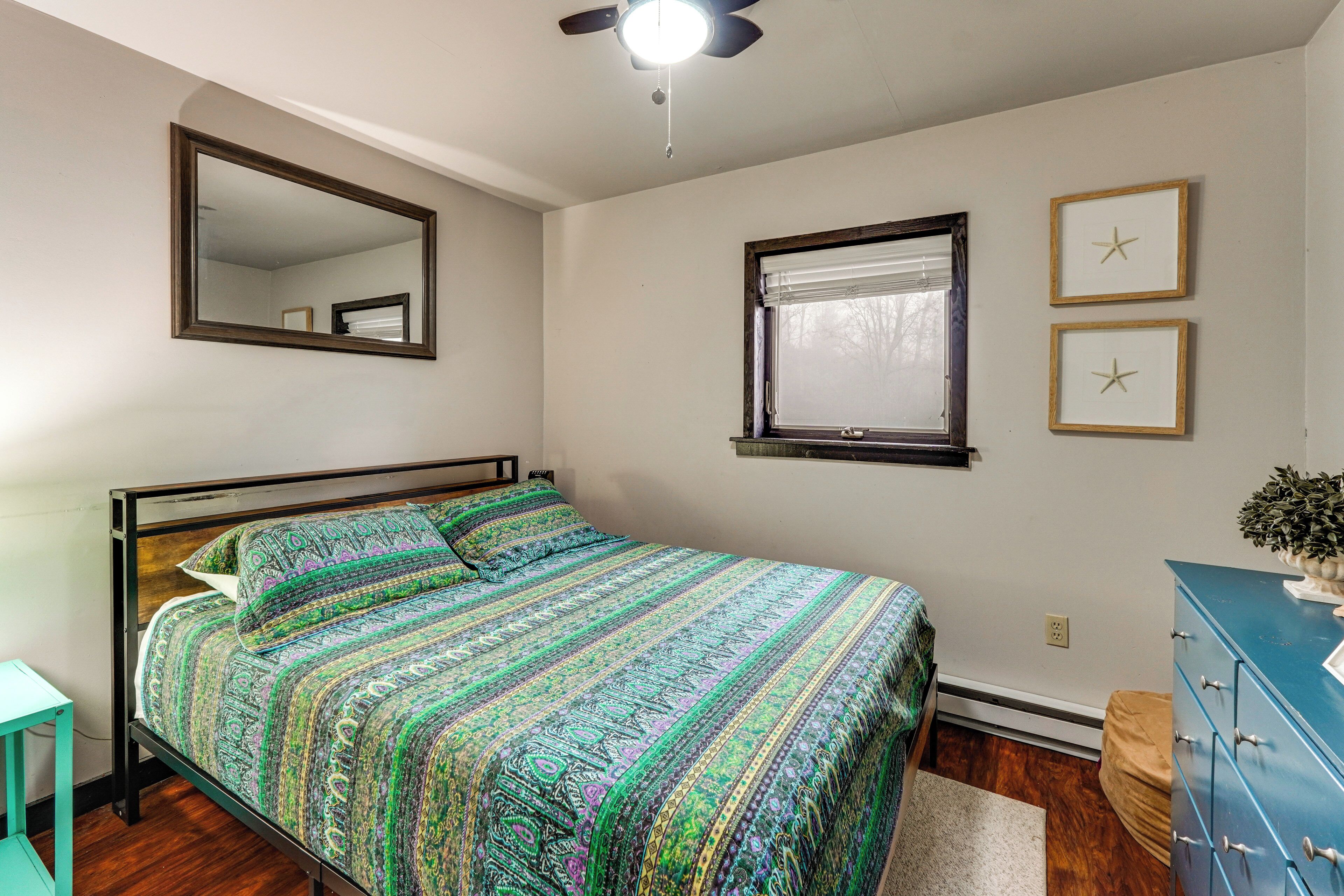 A bedroom with a bed, a ceiling fan, a window with blinds, a dresser, and a mirror on the wall.