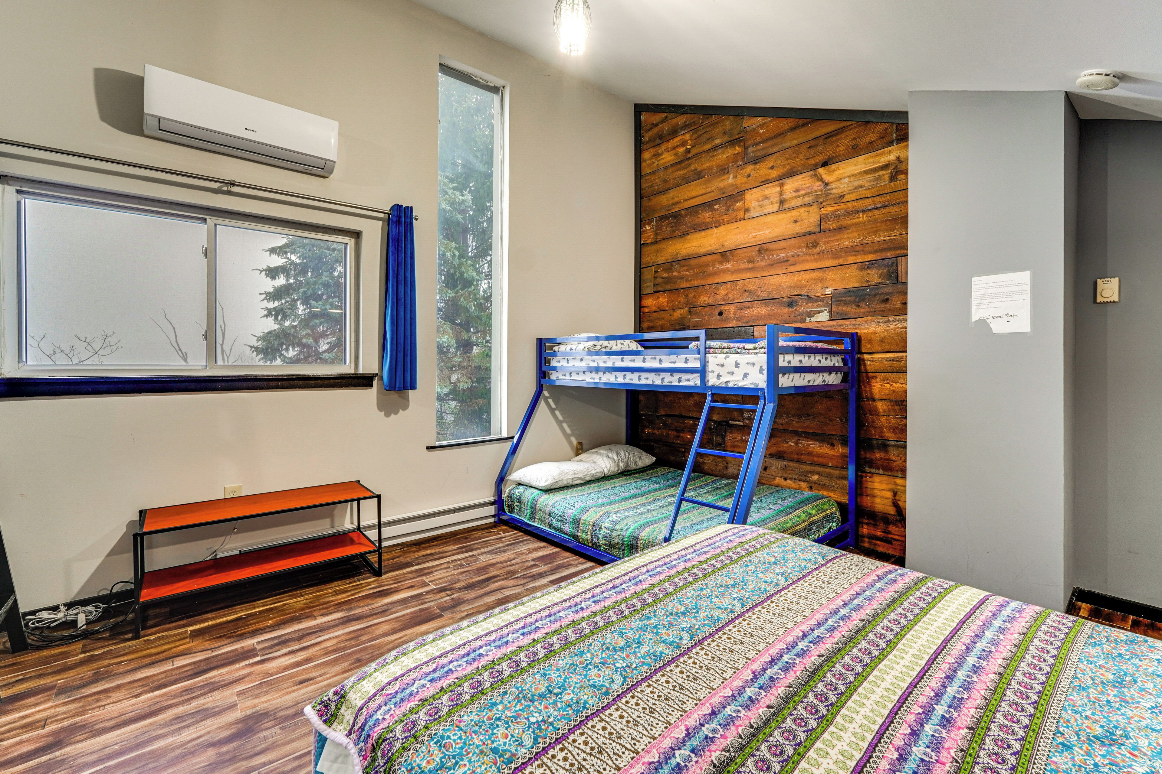 A room with a bunk bed, a bench, a window with curtains, and a wooden wall.