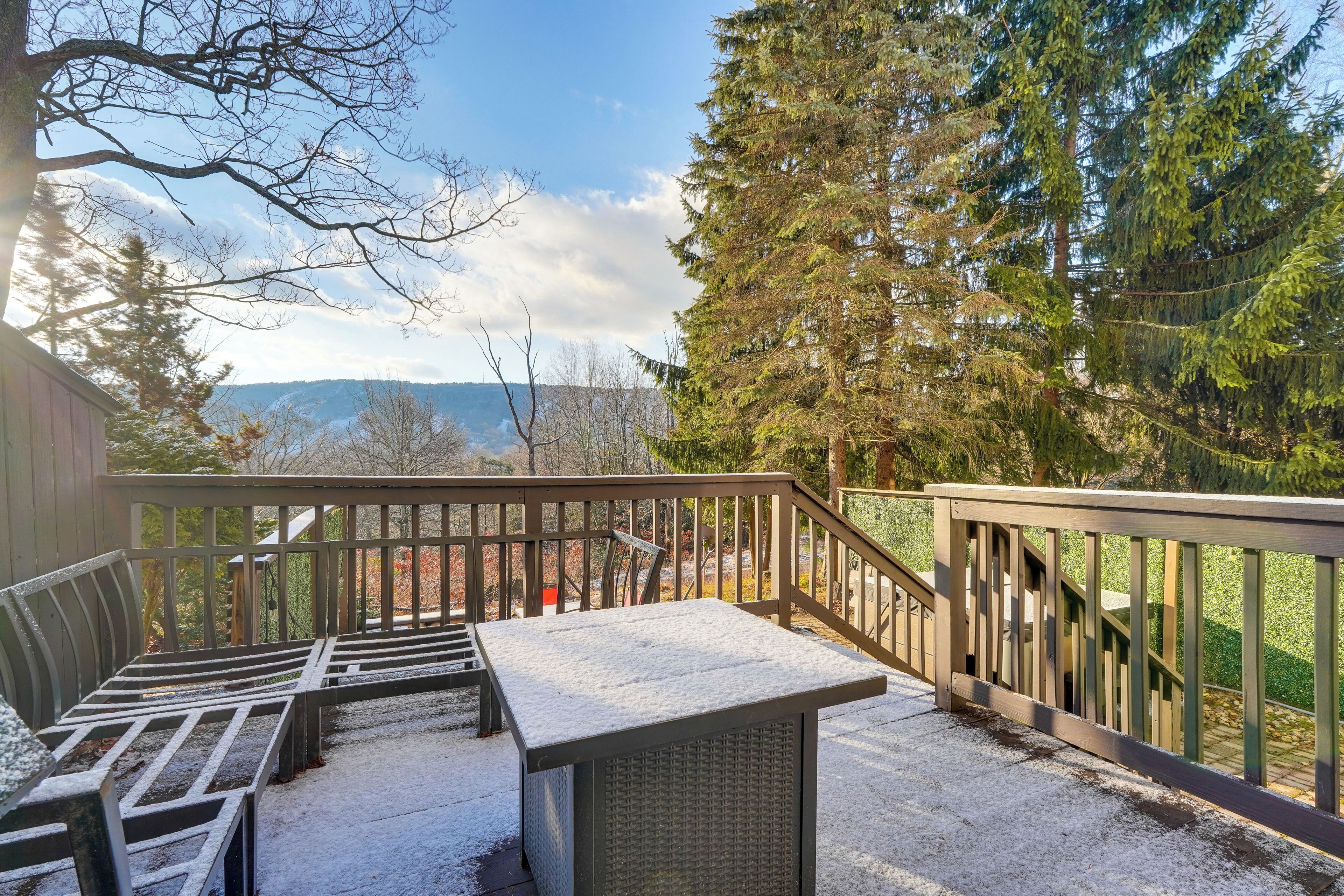 Une terrasse en bois offrant une vue sur les montagnes, un espace salon abrité et une table recouverte de neige.