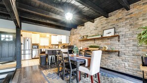 A modern kitchen with stainless steel appliances, a dining area with a patterned rug, and a brick wall with shelves.