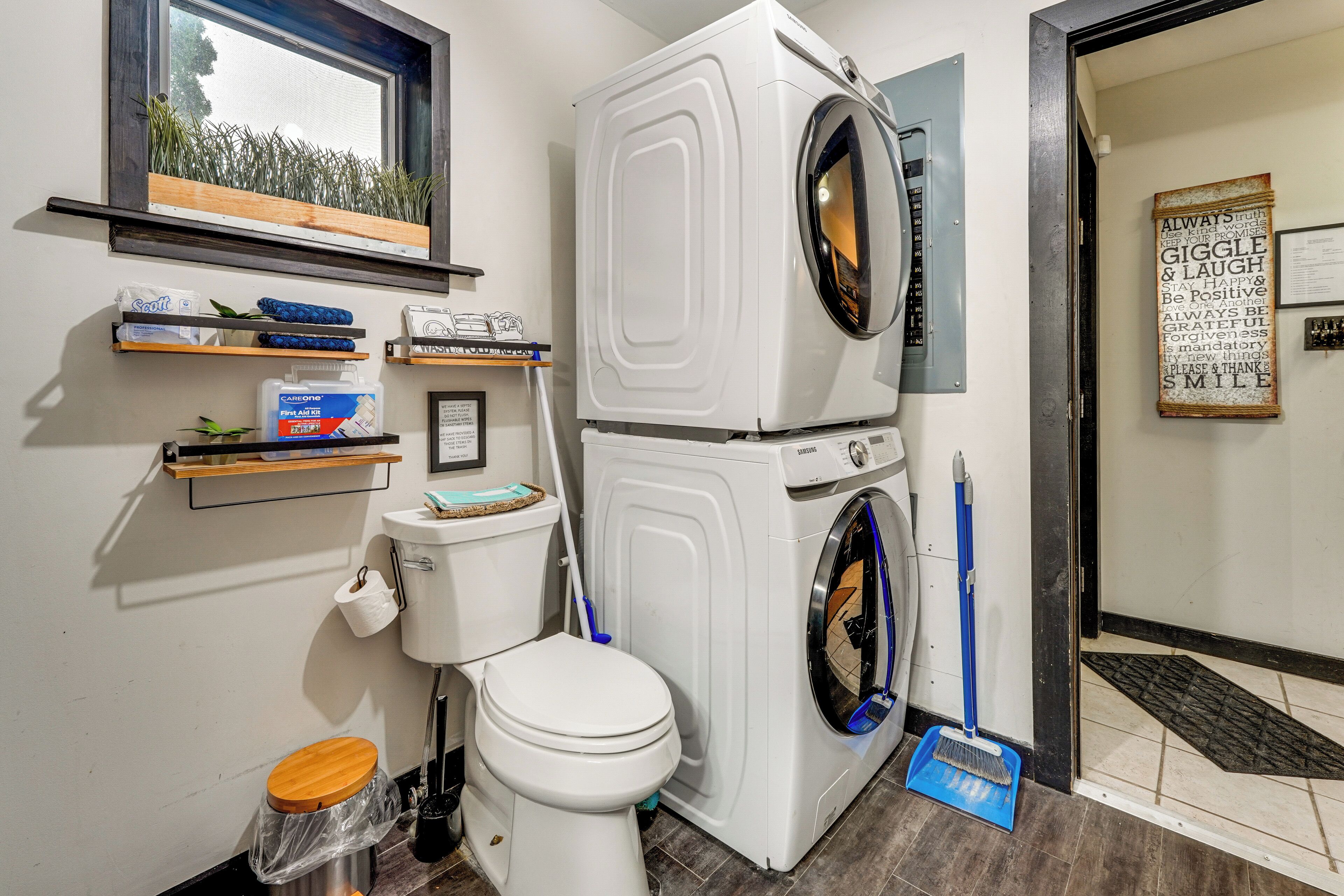 A compact laundry room with a stacked washer and dryer, a toilet, and a broom.