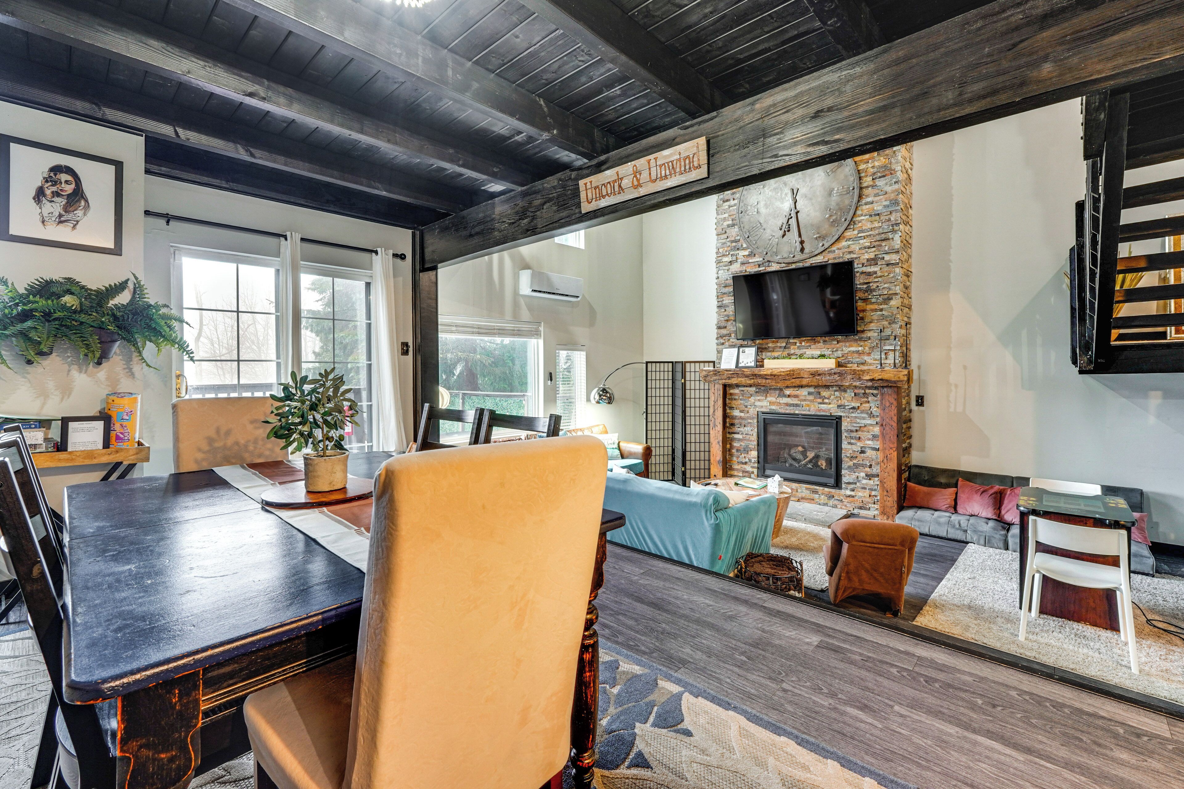 A rustic interior with a dining area, seating, a fireplace, and a large clock on the wall.