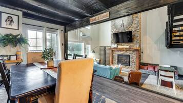 A rustic interior with a dining area, seating, a fireplace, and a large clock on the wall.