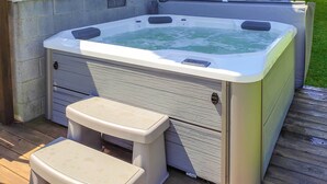A hot tub with two steps and a control panel, situated on a wooden deck.