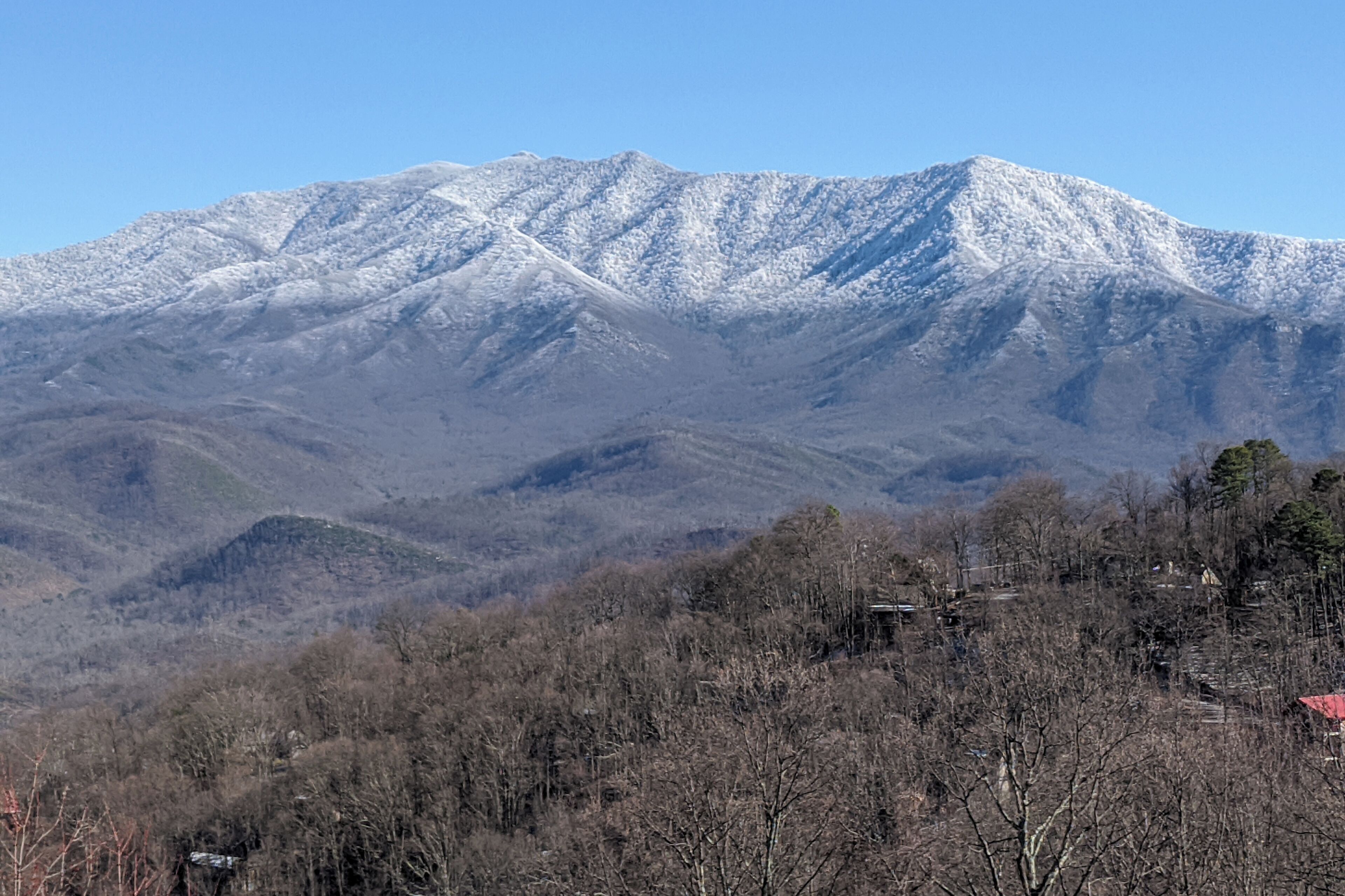 Une chaîne de montagnes aux sommets enneigés, surplombant une vallée boisée.