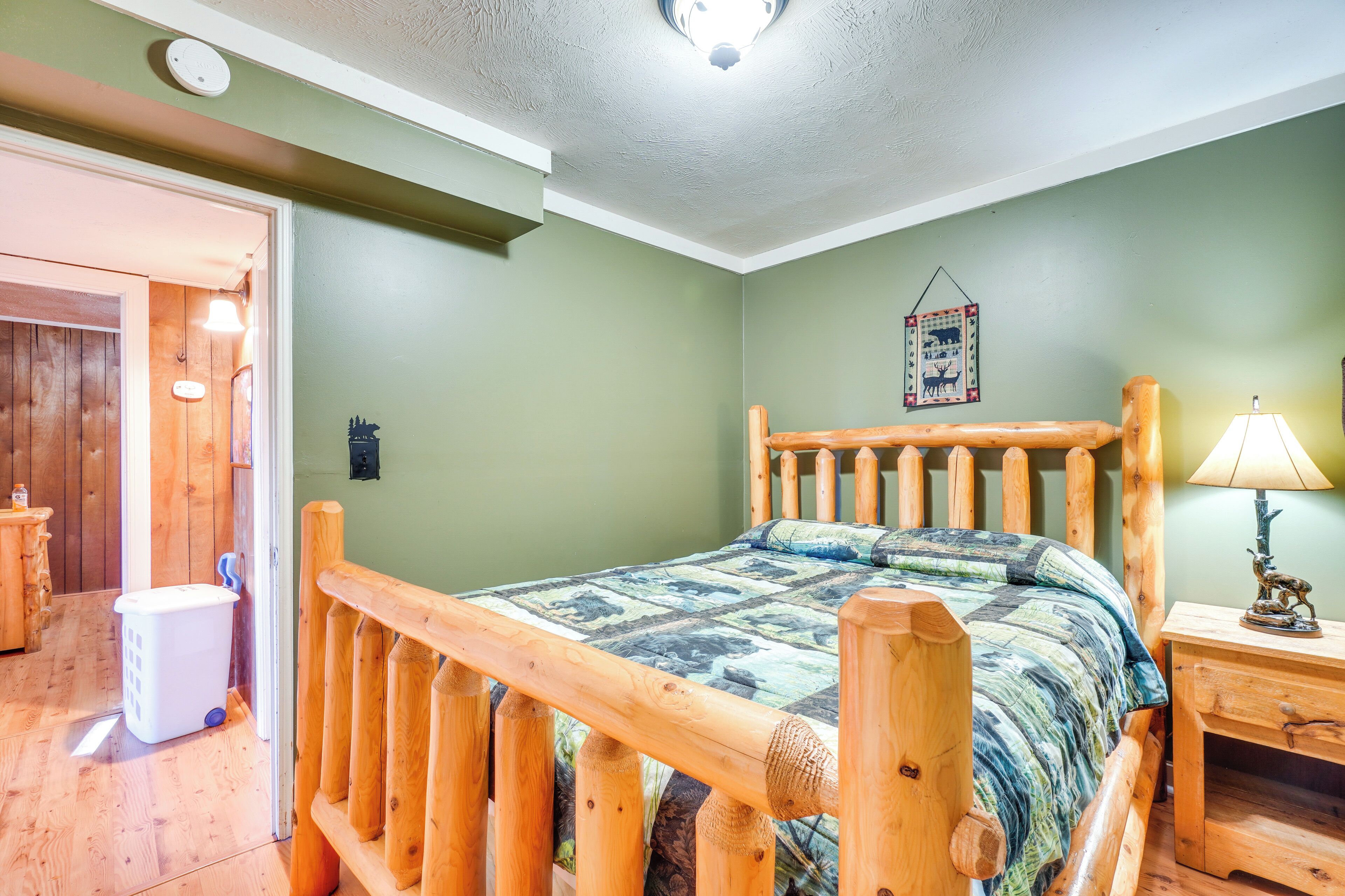 Una cama de madera con colcha, una mesita de noche con lámpara y un tapiz en la pared.