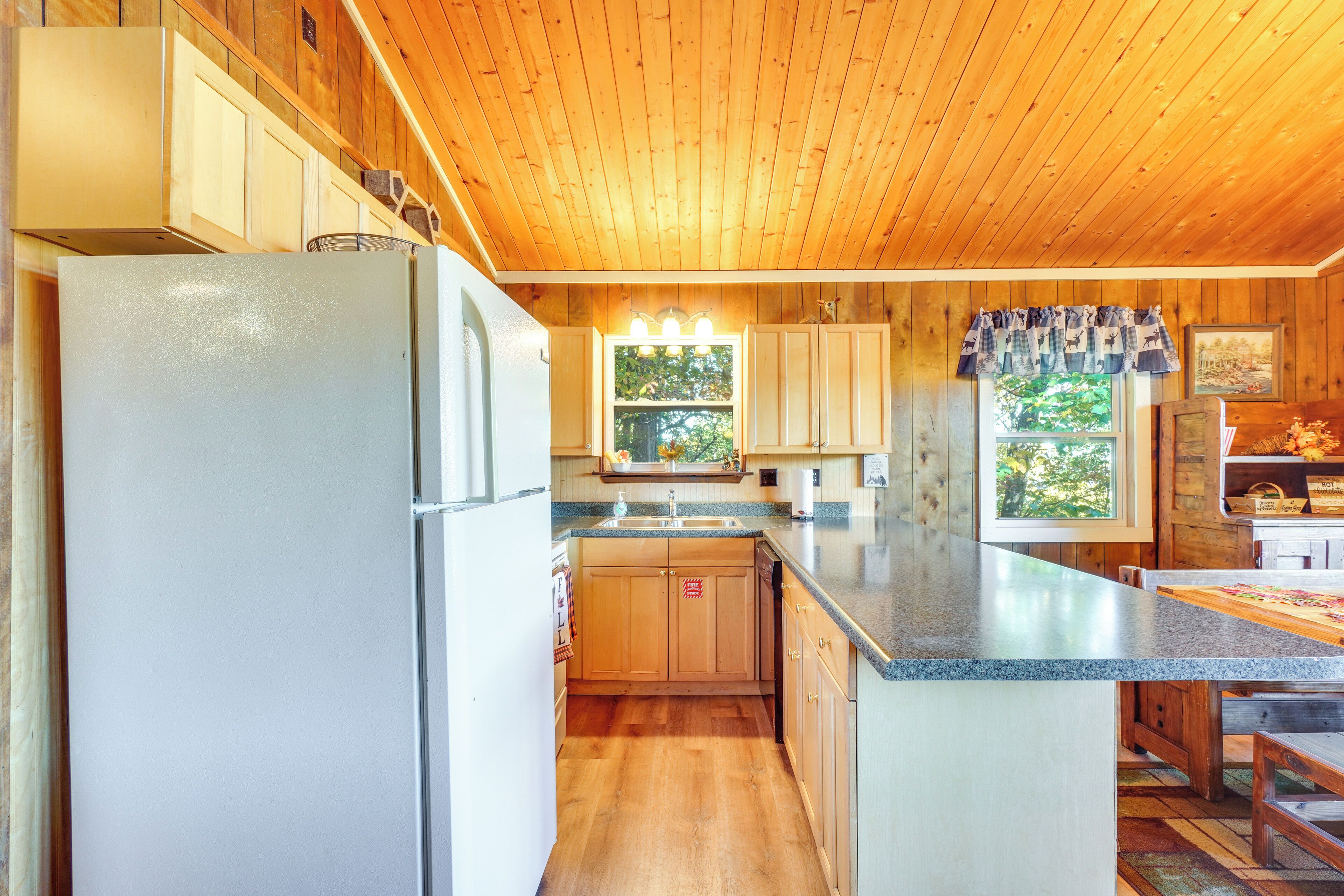 Una cocina con armarios de madera, un refrigerador, un lavamanos y un ventanal con vistas a árboles.