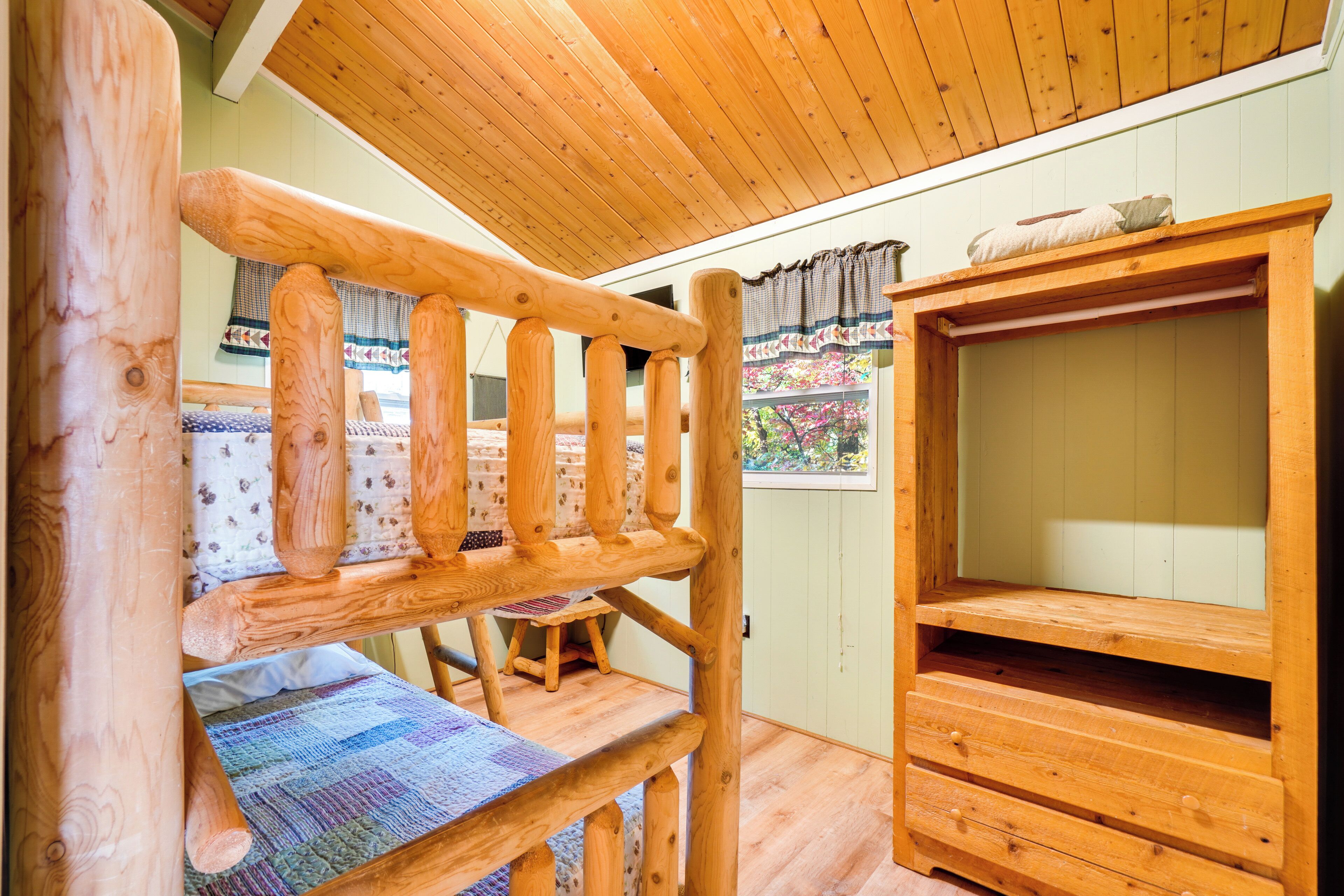 Una cama nido de madera con colchón acolchado, un mueble de madera con televisor y una ventana con cortinas.