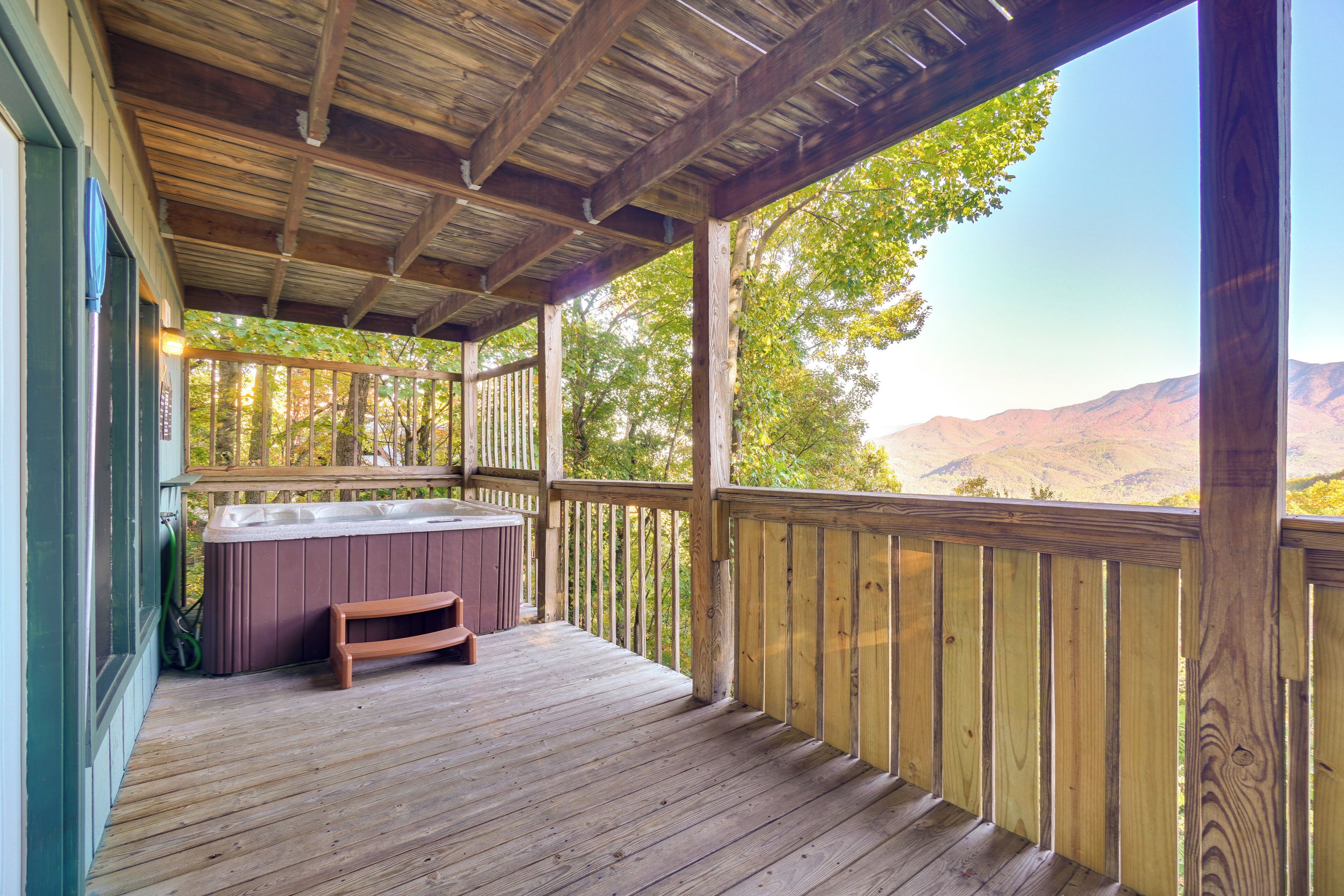 A wooden deck with a hot tub and a bench, overlooking a mountainous landscape.