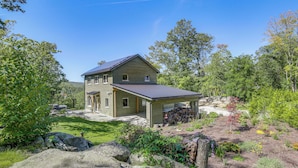 A two-story house with a covered porch, surrounded by a well-maintained garden and large rocks. - 'the Glabin: Garrison Gem w/ Hot Tub & Fire Pit (Garrison)