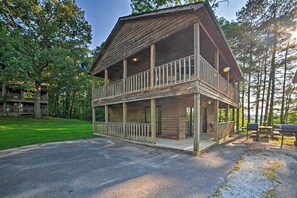 A two-story wooden cabin with a balcony, surrounded by trees and a gravel driveway. - Group-friendly Cabin on Kentucky Lake! (Springville)
