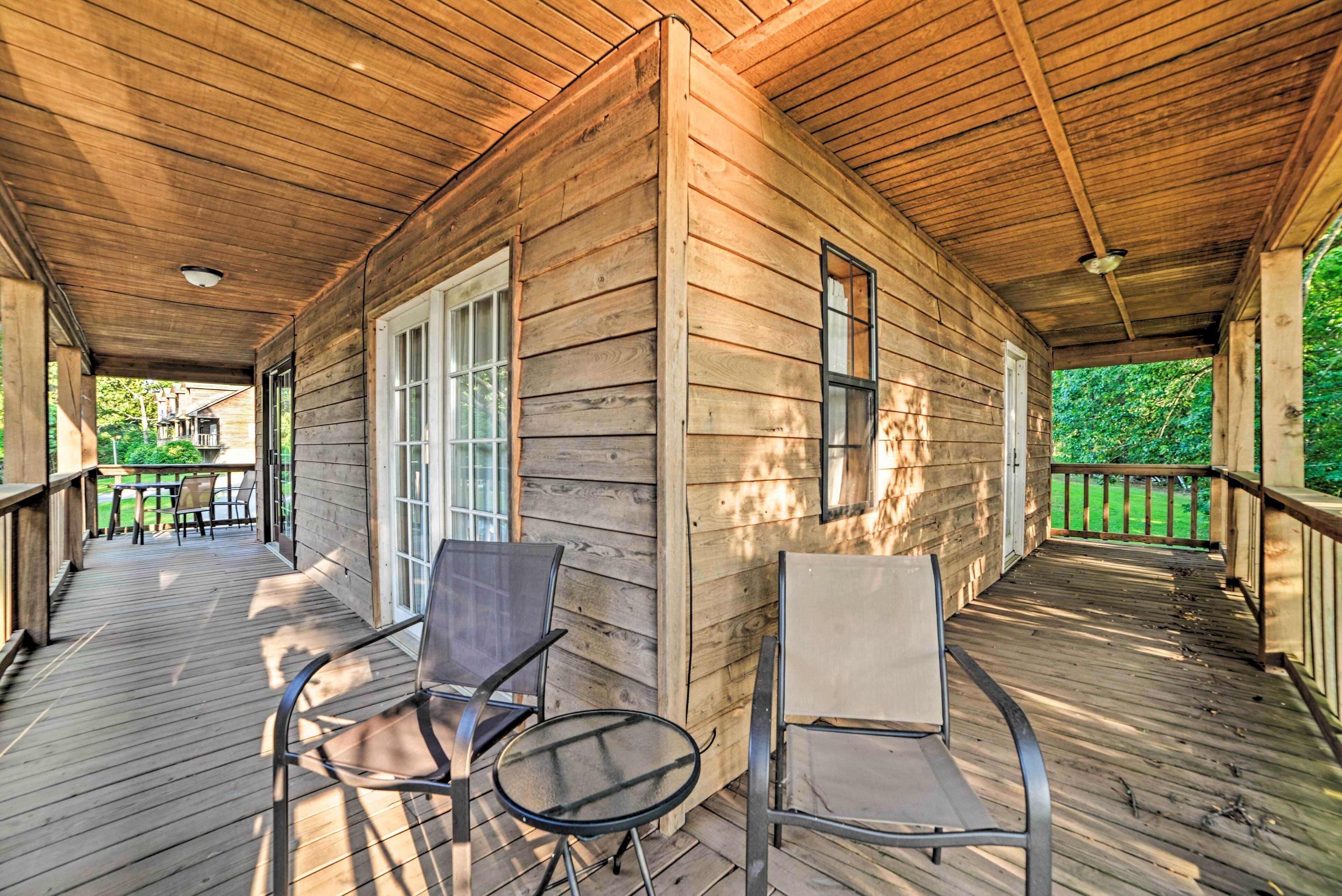 A wooden cabin with a covered porch, two chairs, and a table.