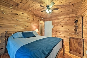 A wooden-paneled bedroom with a bed, a ceiling fan, and a door. - Group-friendly Cabin on Kentucky Lake! (Springville)