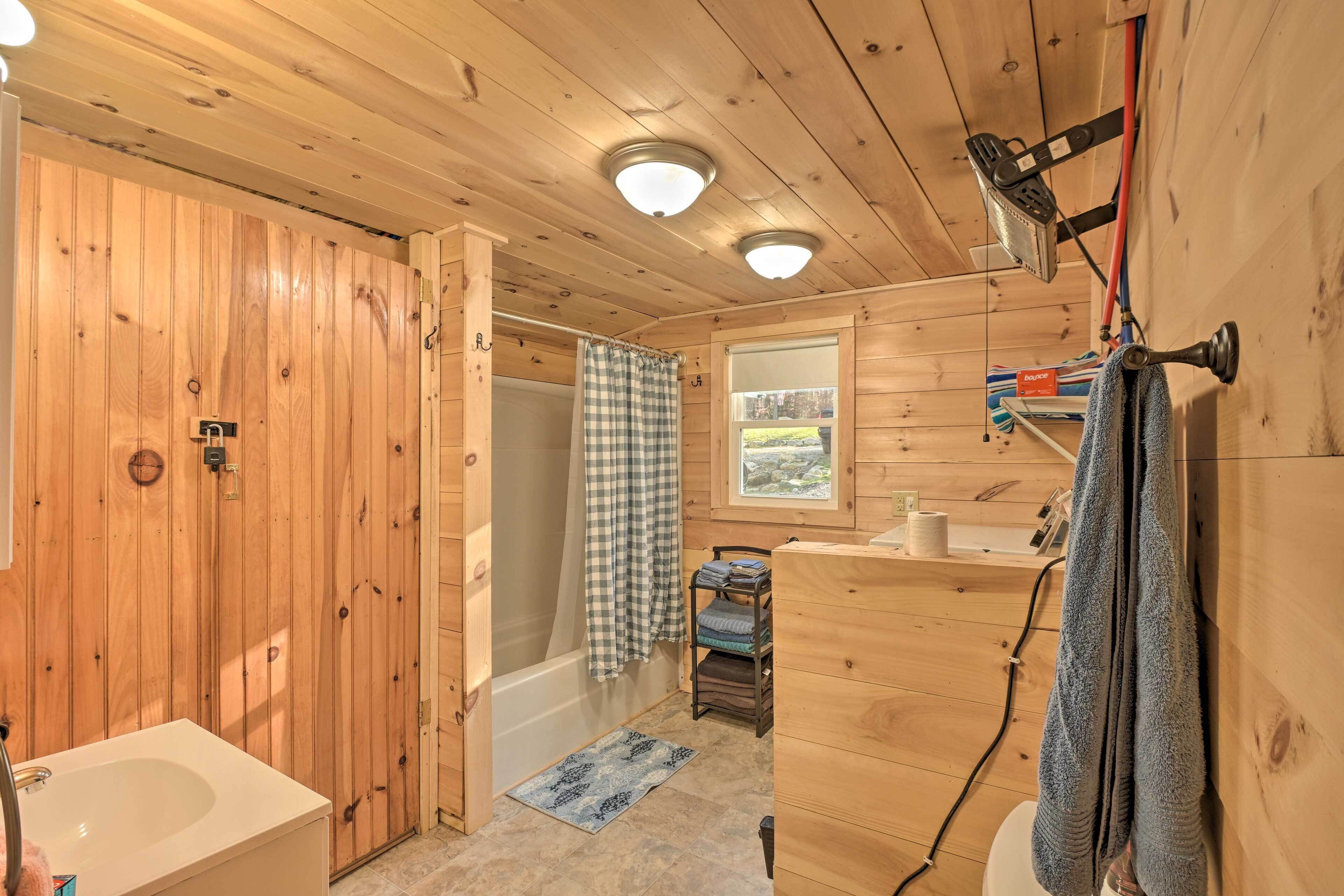 A wooden cabin bathroom with a bathtub, a toilet, a sink, and a window.