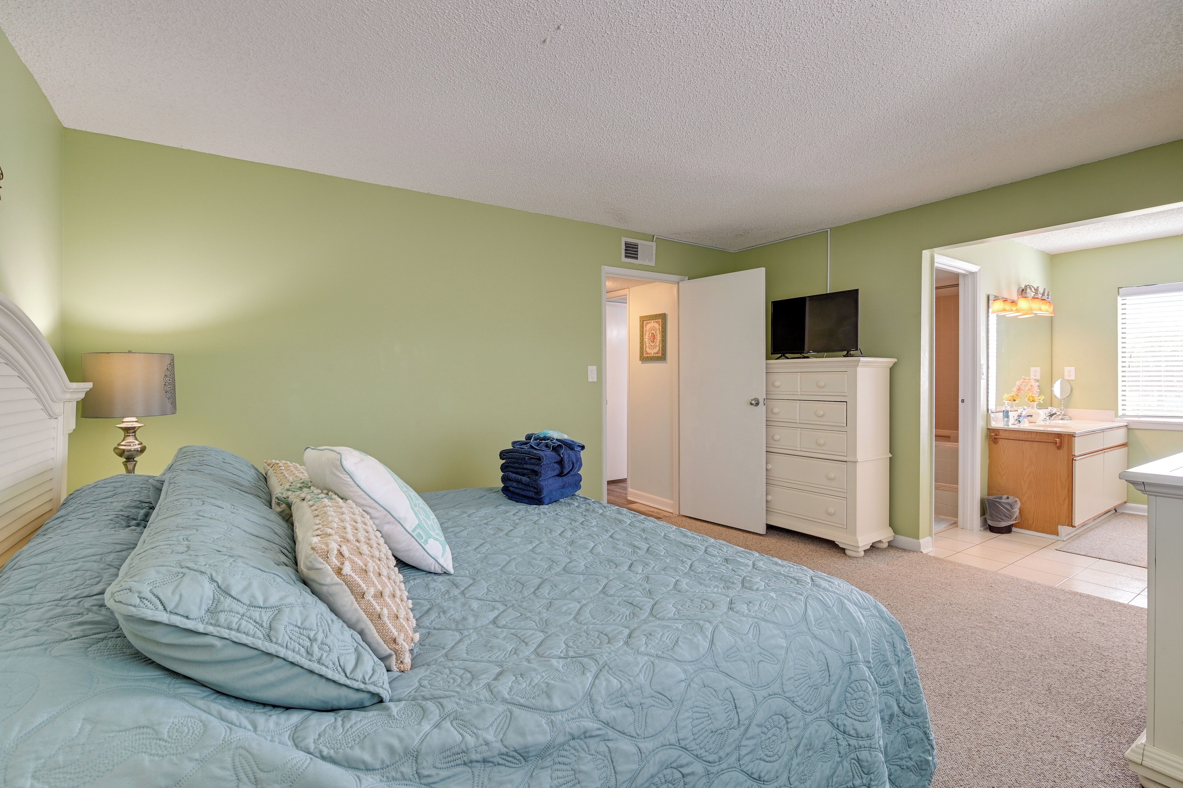 A bedroom with a bed, a dresser, a television, and a bathroom visible through an open door.