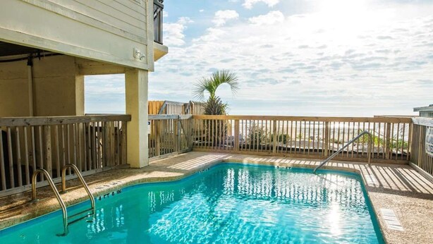 Piscina com deck de madeira e vista para o oceano.