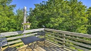 A wooden deck with a table and chairs, surrounded by lush greenery. - Charming Studio ~ 20 Mi to Acadia Nat'l Park! (Ellsworth)