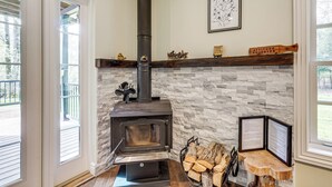 A stone fireplace with a black chimney, a mounted sign, and a log holder. - Poconos Cottage w/ Sauna ~ 10 Mi to Camelback! (Tobyhanna)