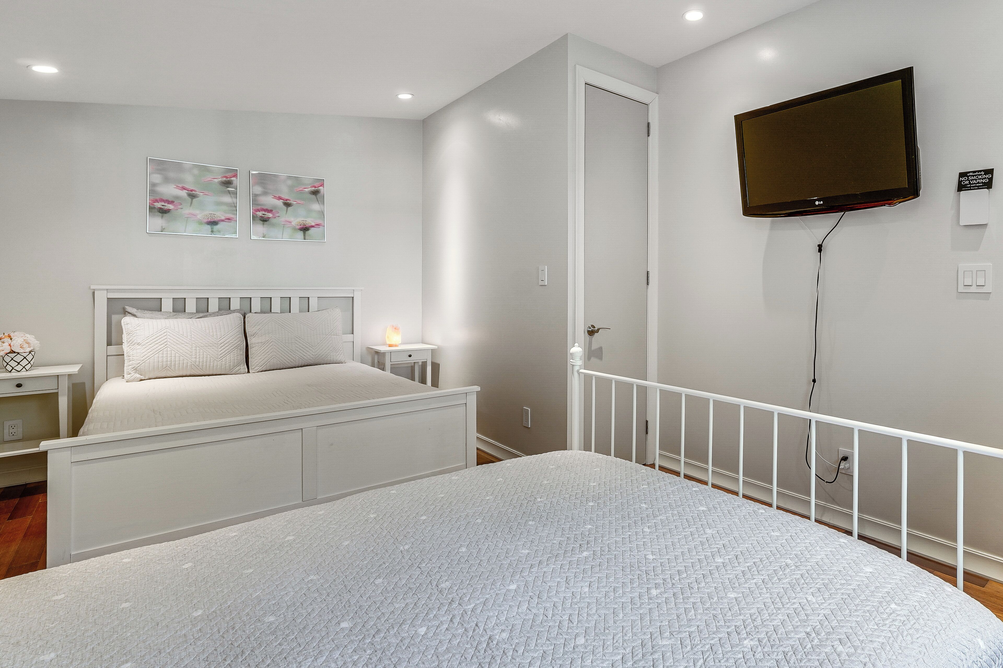 A bedroom with a bed, a nightstand, a wall-mounted TV, and two wall art pieces.