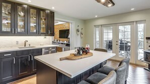 A modern kitchen with dark cabinets, a large island, and a dining area with bar stools. - Poconos Cottage w/ Sauna ~ 10 Mi to Camelback! (Tobyhanna)