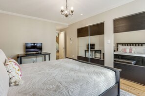 Un dormitorio con cama, televisor, cómoda, espejo y candelabro.