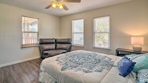 A bedroom with a bed, a chair, a ceiling fan, and three windows.